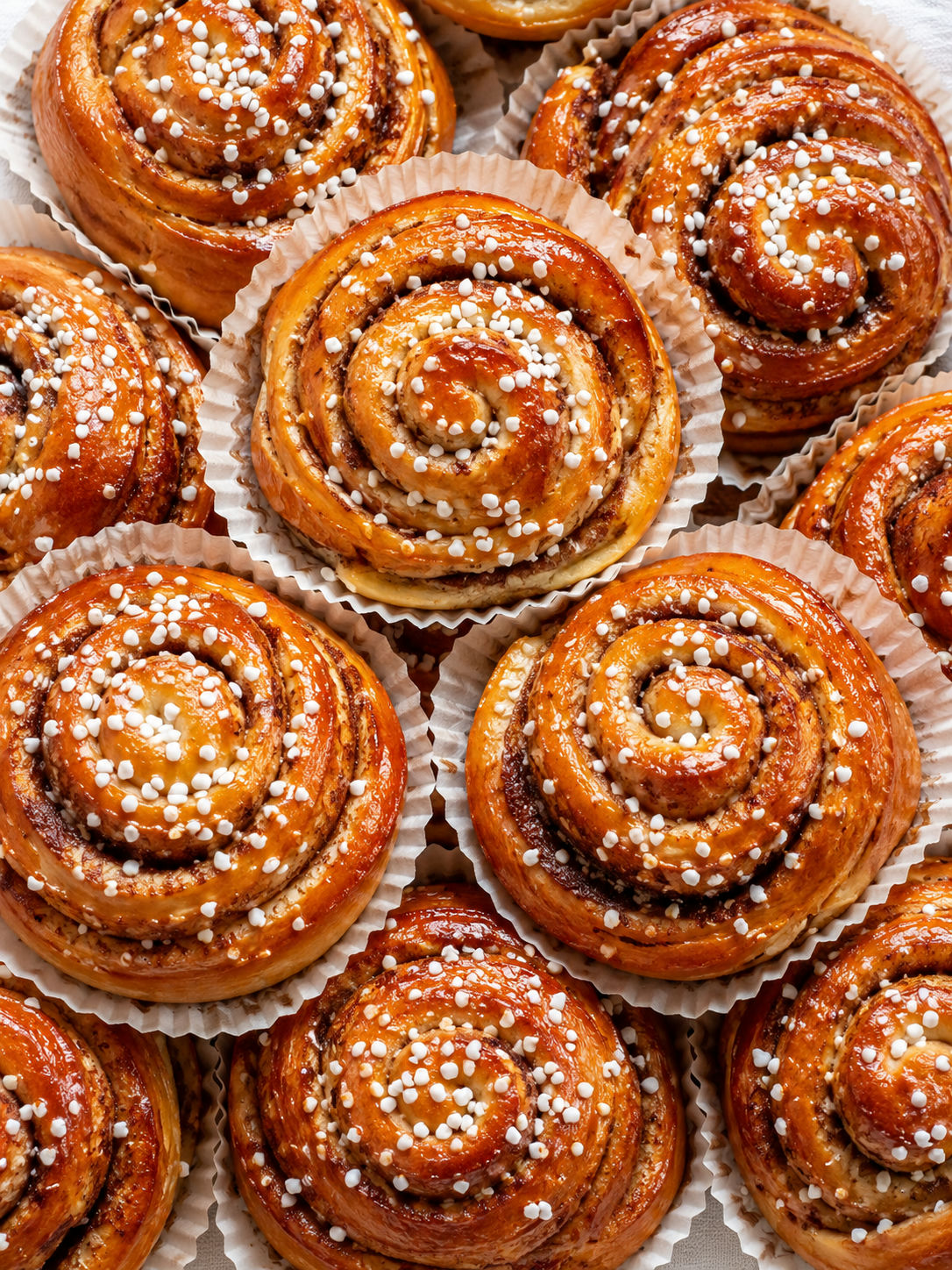 Kanelbullar med pärlsocker sedda ovanifrån på vitt linne