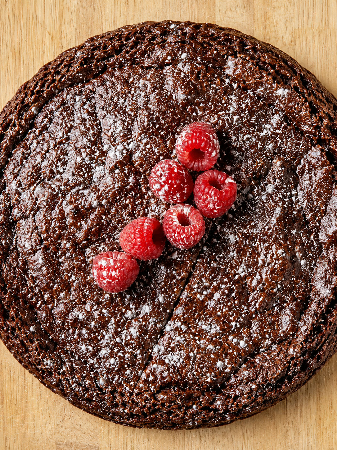 Hel kladdkaka med florsocker och hallon sedd uppifrån